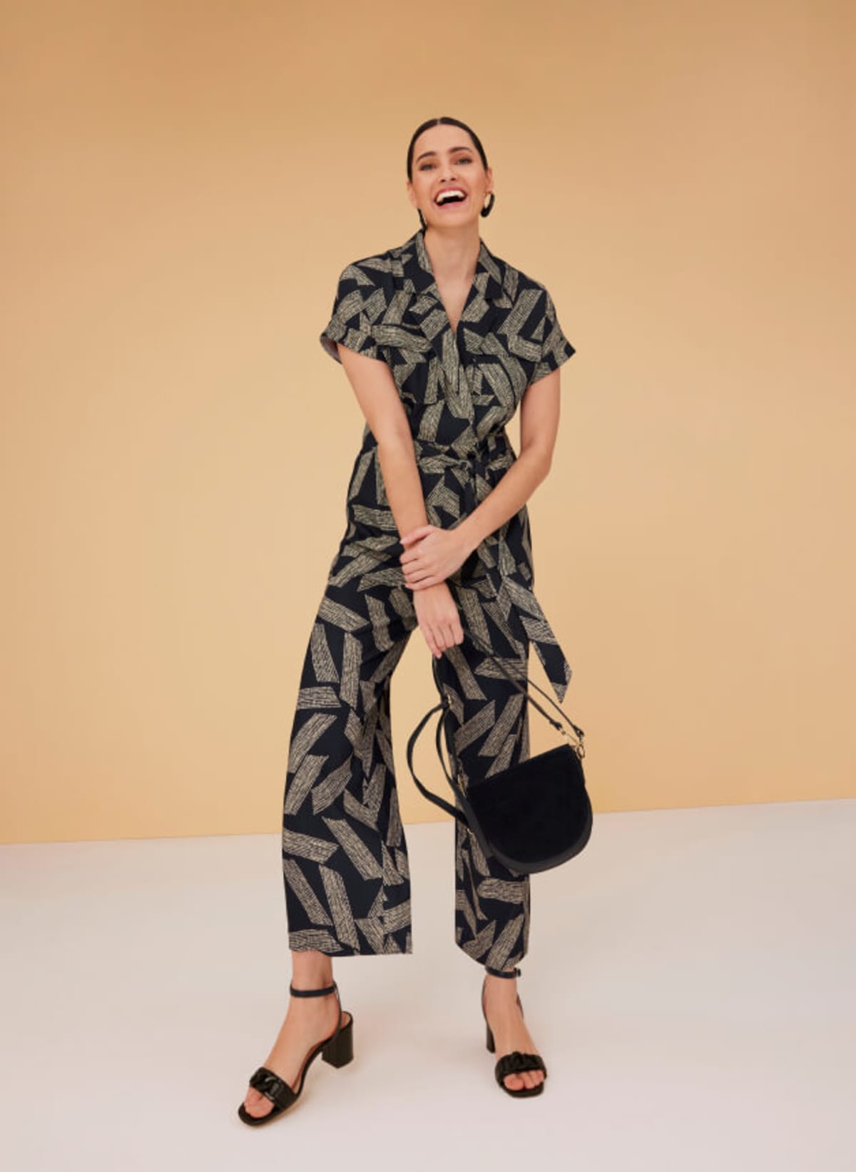 Woman wearing abstract print jumpsuit with black bag and heeled sandals