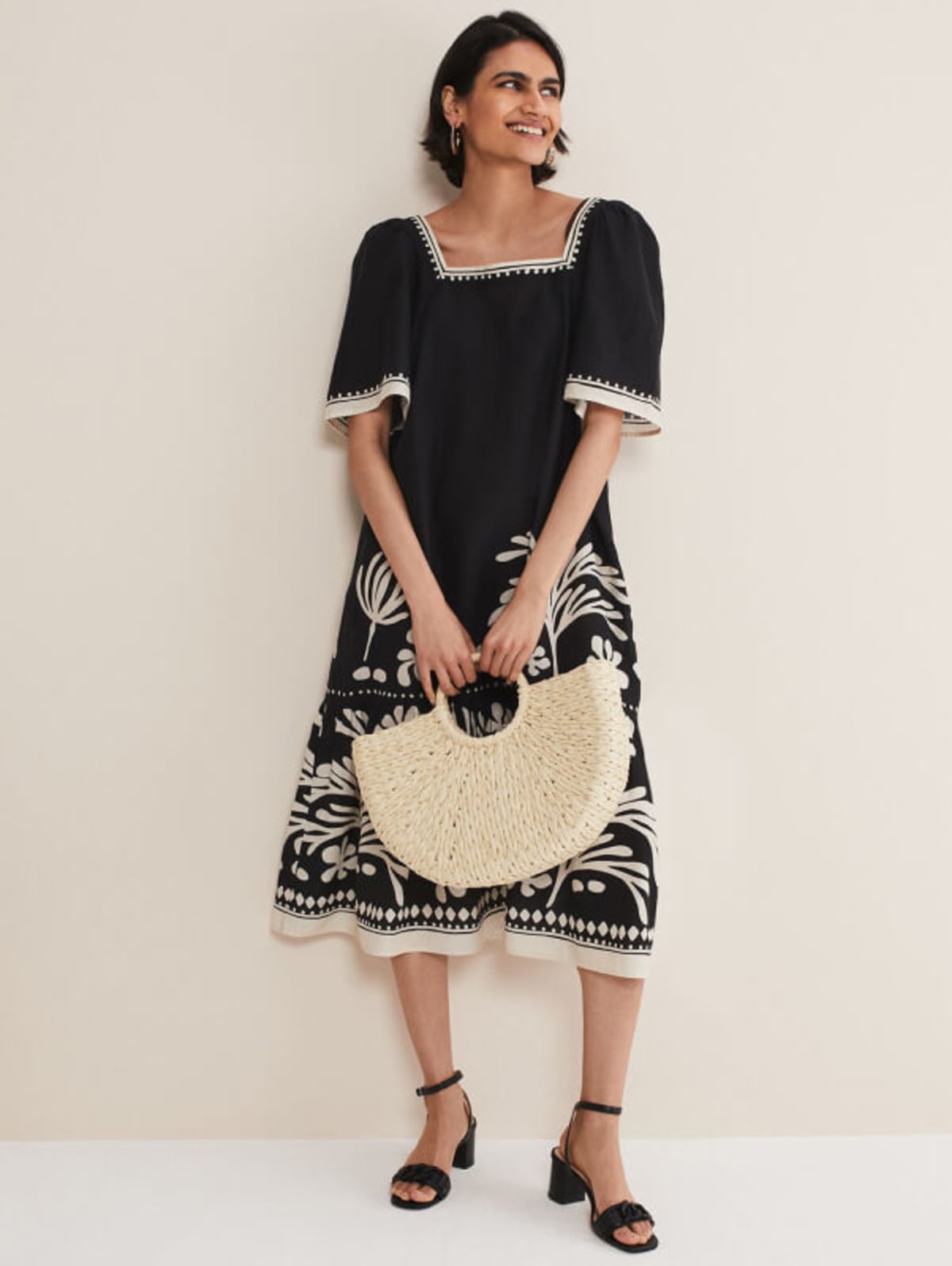 Woman wearing black linen dress with a straw bag and black sandals