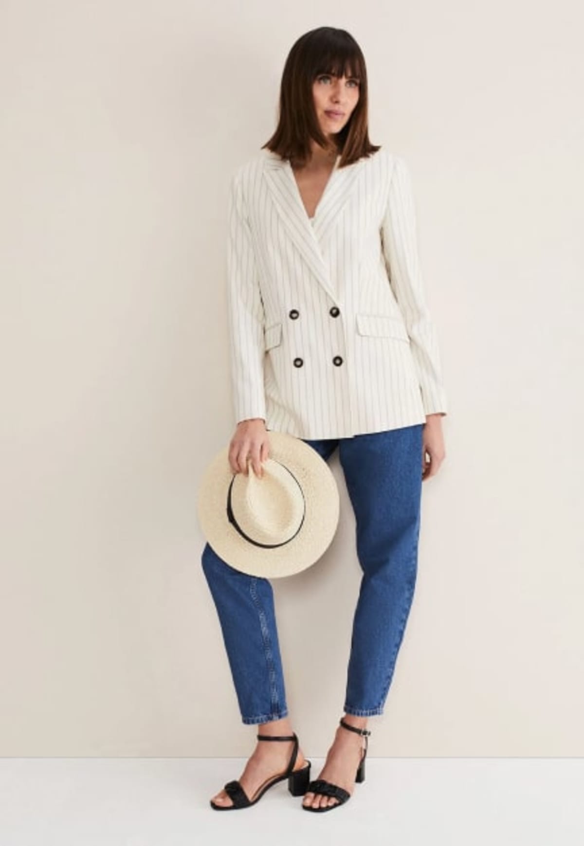 Woman wearing striped suit blazer with blue jeans and a straw hat